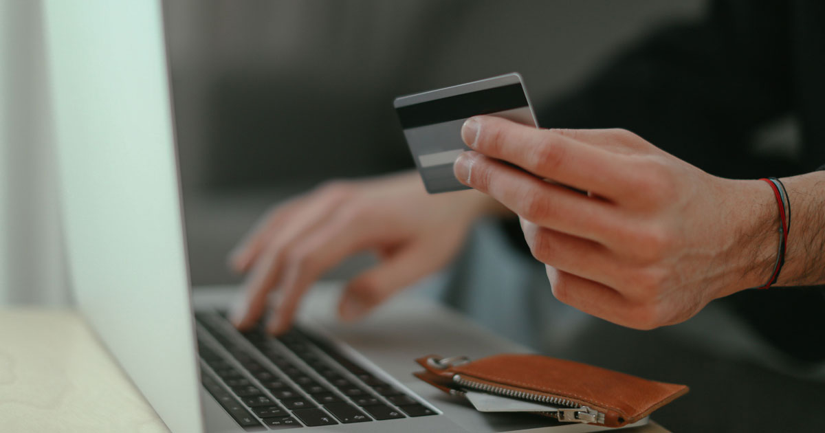 A person holding a credit card while typing on a laptop computer representing secure transactions to sell USDT Dubai safely